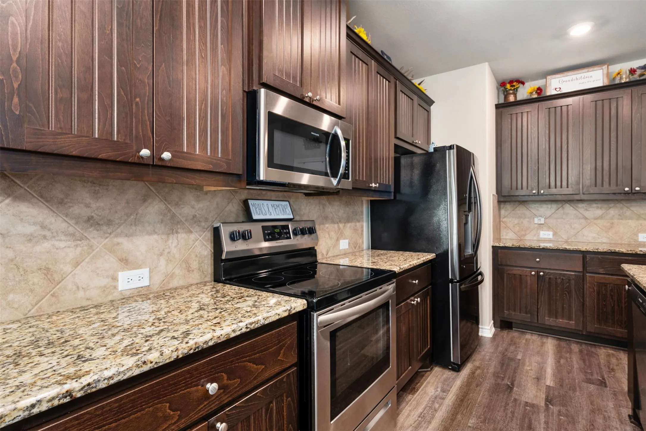 Kitchen featuring wood-finish cabinetry, granite countertops, tile backsplash, stainless steel appliances, and wood-finish flooring