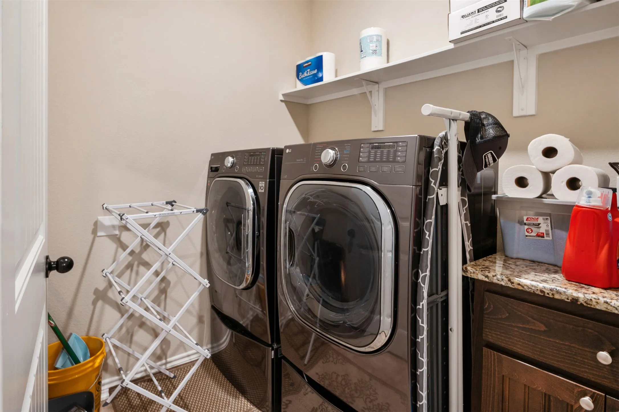 Dedicated laundry area featuring a patterned carpet, built-in shelving, a granite-finish countertop, and dark wood cabinetry