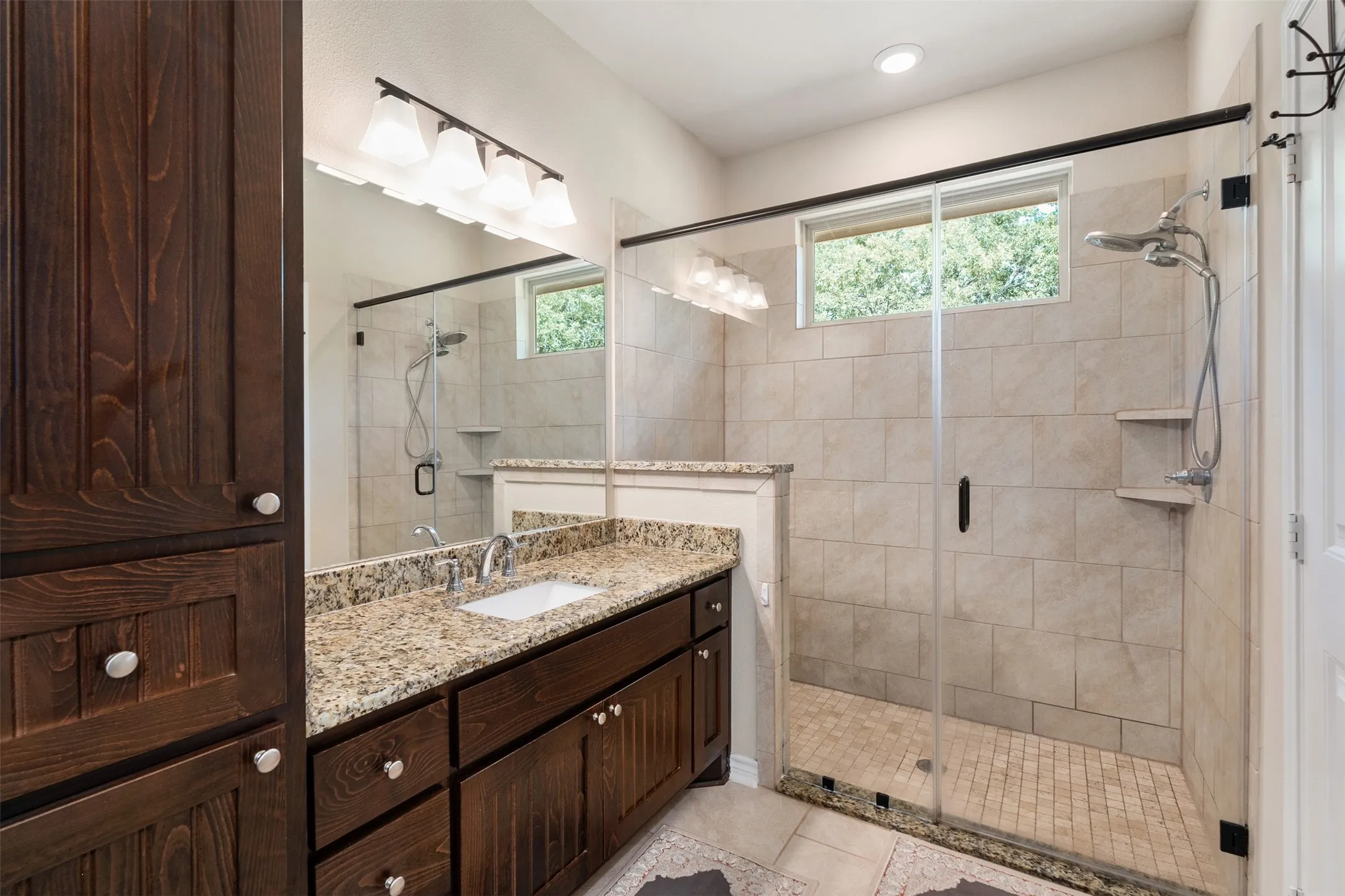 Spacious bathroom featuring a glass-enclosed shower, a large vanity with a granite countertop, and extensive dark wood-finish cabinetry