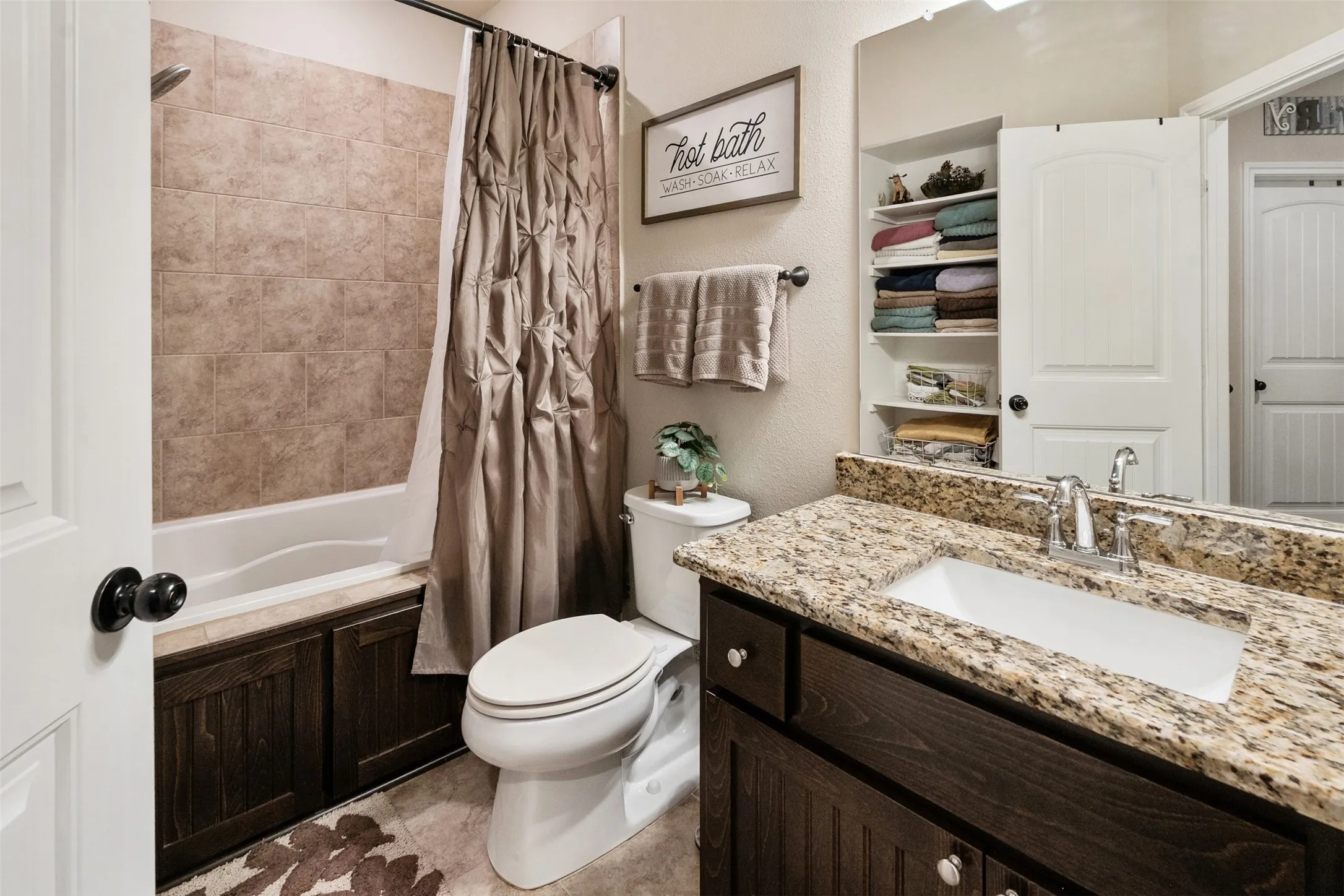 Bathroom featuring a bathtub with tile surround, a built-in dark wood vanity with granite countertop and undermount sink, and recessed shelving