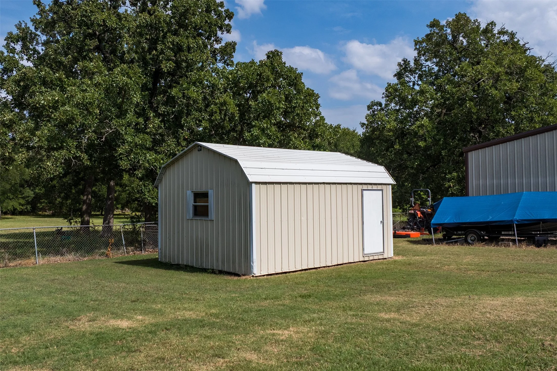 Utility shed featuring a white arched metal roof, light-colored vertical metal siding, and a single window