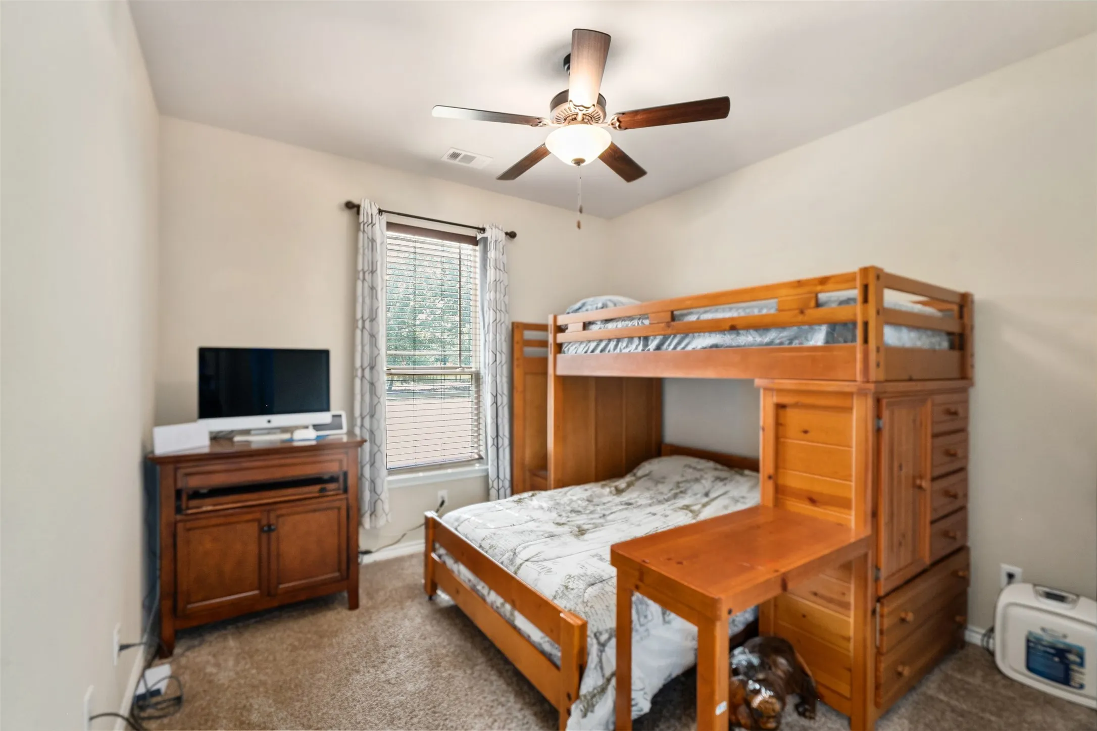 Light-colored walls and carpet flooring complement the natural light from a window with blinds