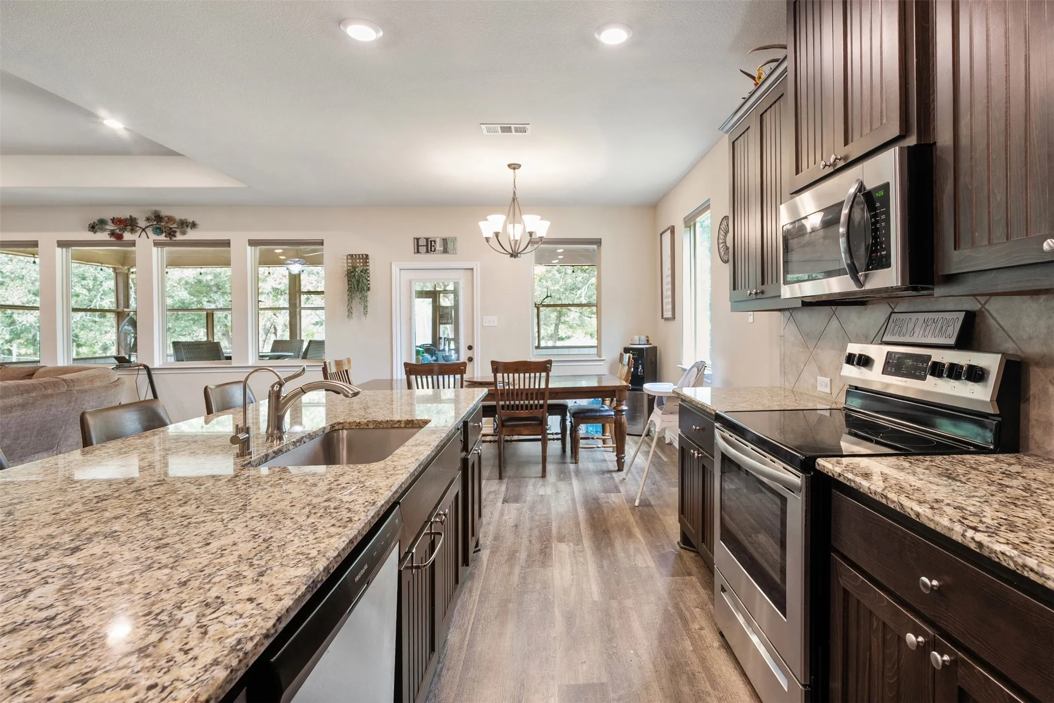 Kitchen featuring a large central island with an undermount sink, granite countertops, wood-finish flooring, dark wood cabinetry, and stainless steel appliances