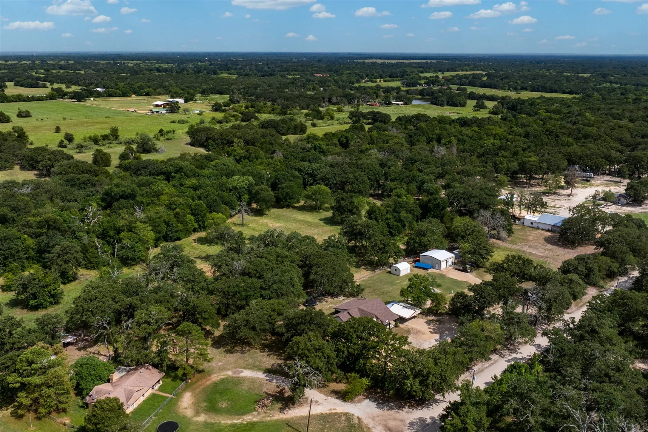 Expansive rural landscape featuring a mix of dense tree cover and open fields, showcasing several residential structures and outbuildings