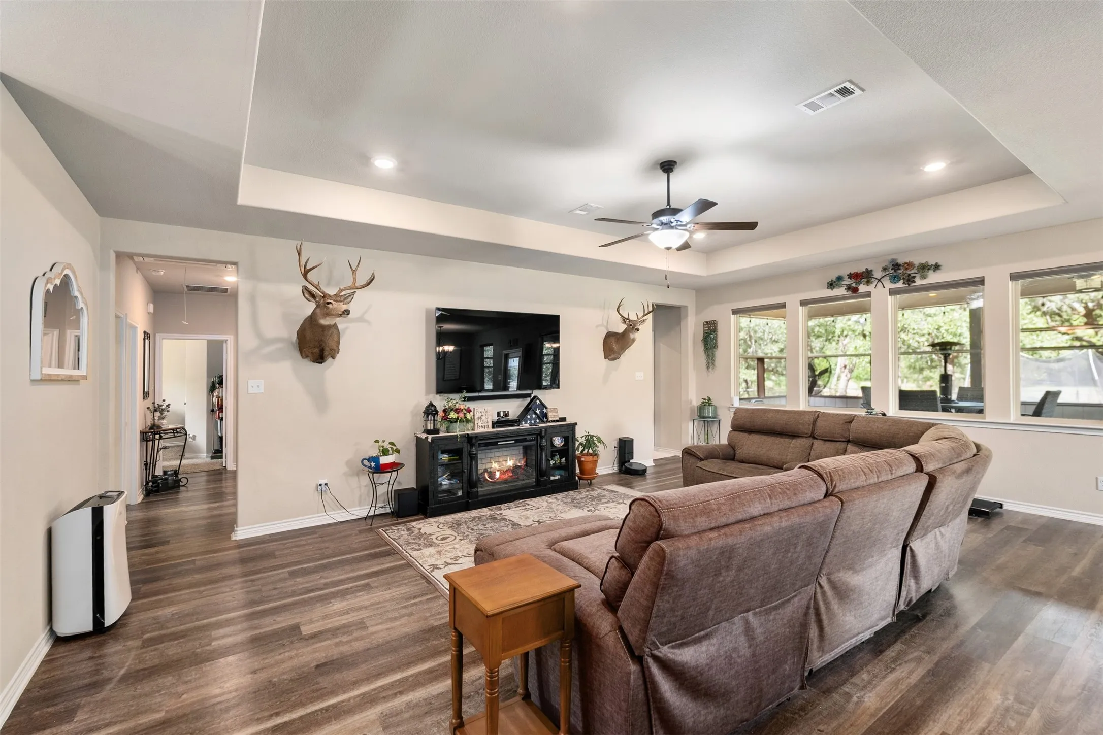Spacious living area featuring wood-finish flooring, a tray ceiling with recessed lighting, and a ceiling fan
