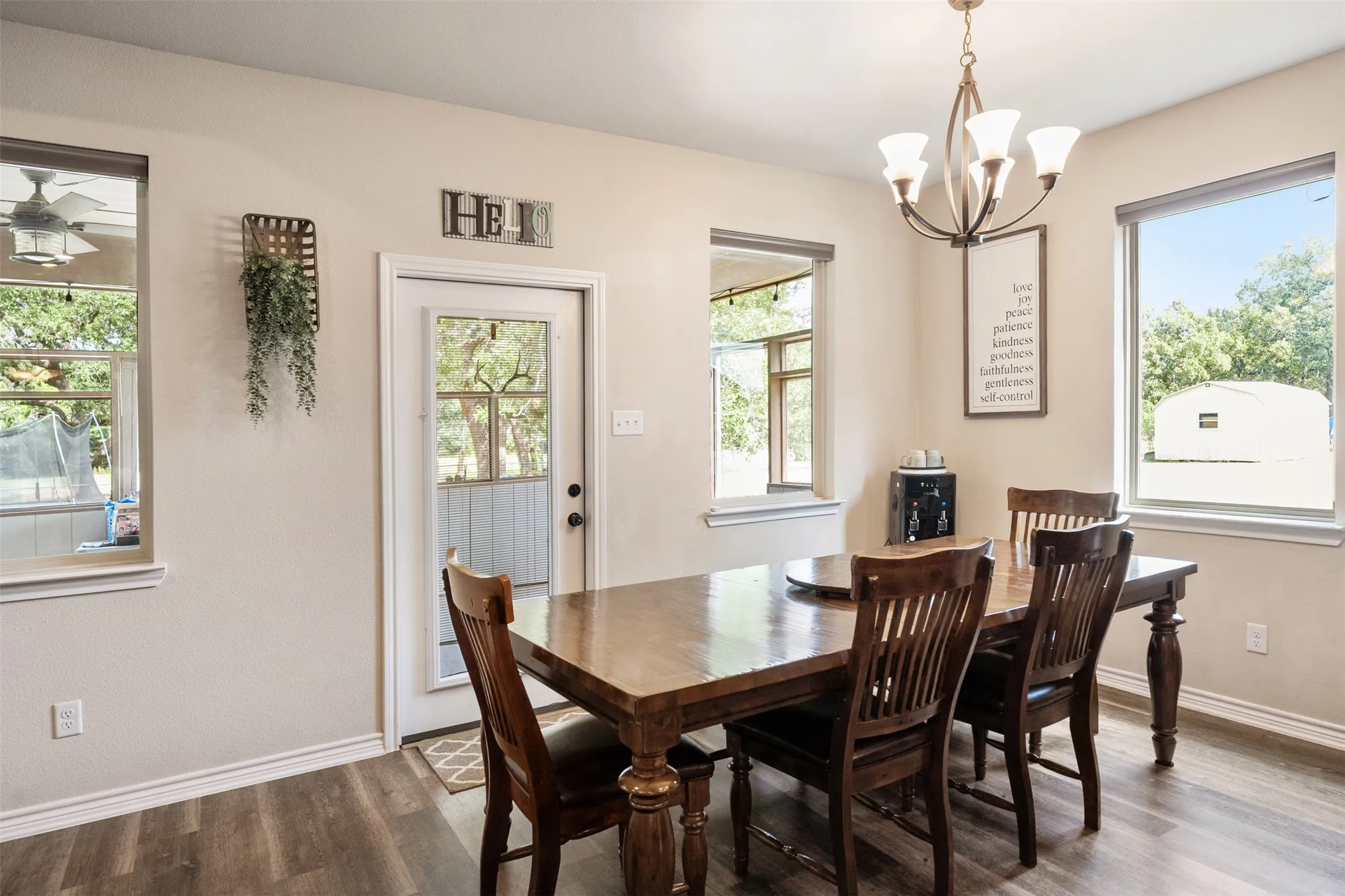 Dining area featuring wood-finish flooring, a contemporary chandelier, multiple windows with white trim, and a glass-paneled door