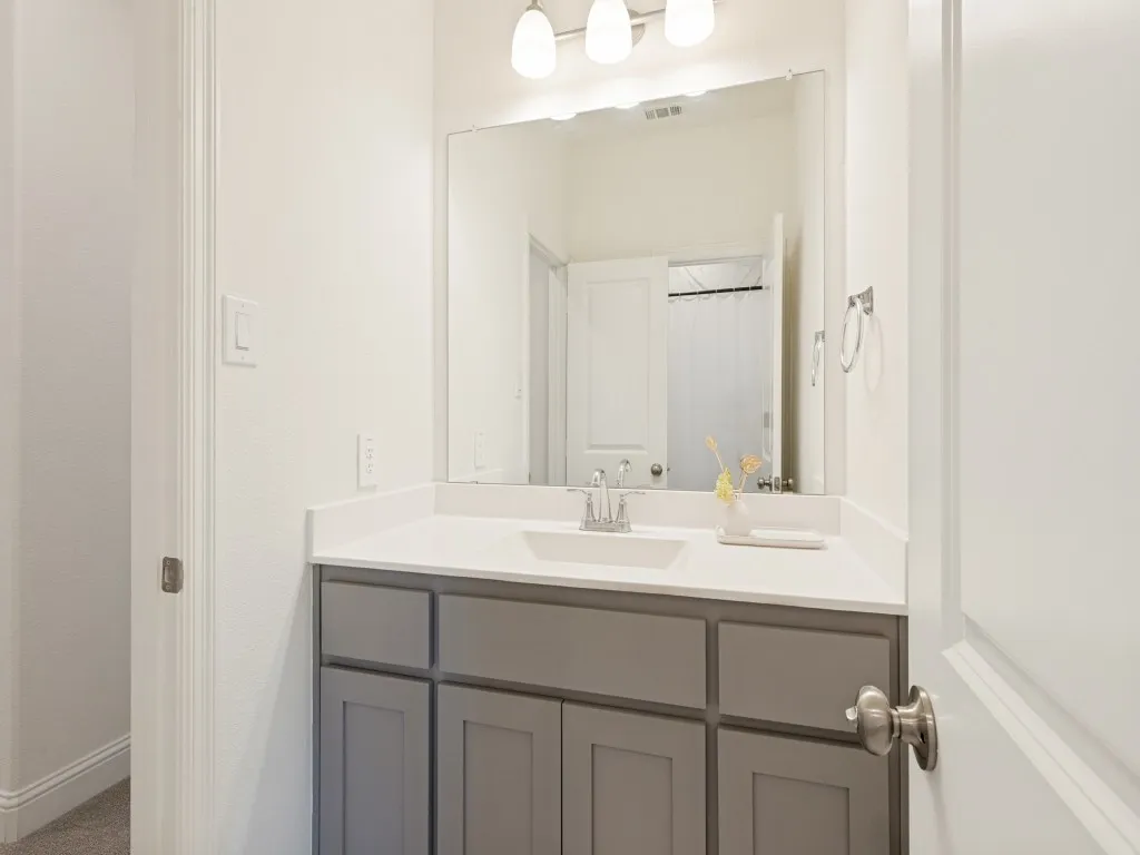 Bathroom featuring a single vanity with gray shaker-style cabinetry, a white countertop, an integrated rectangular sink, and a framed mirror