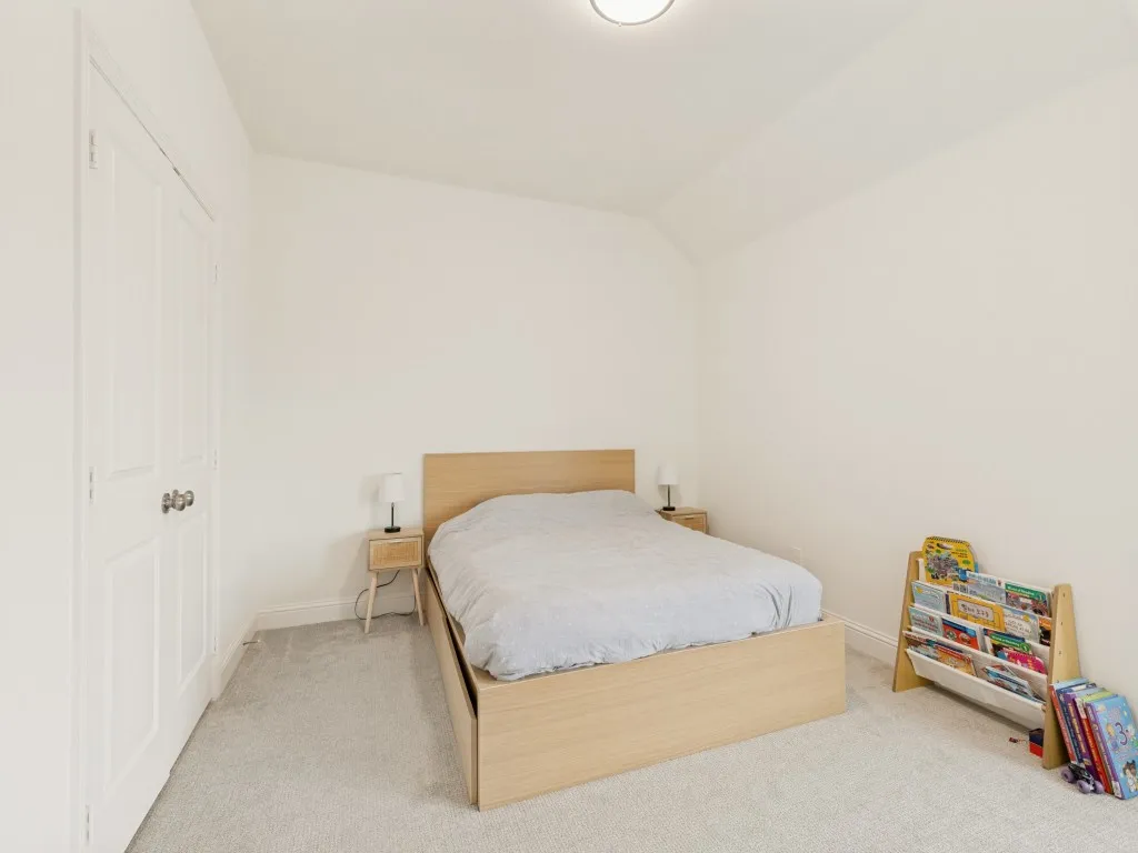 Bedroom featuring light neutral carpeting, white painted walls, a flat ceiling light fixture, and white bi-fold closet doors with brushed nickel hardware