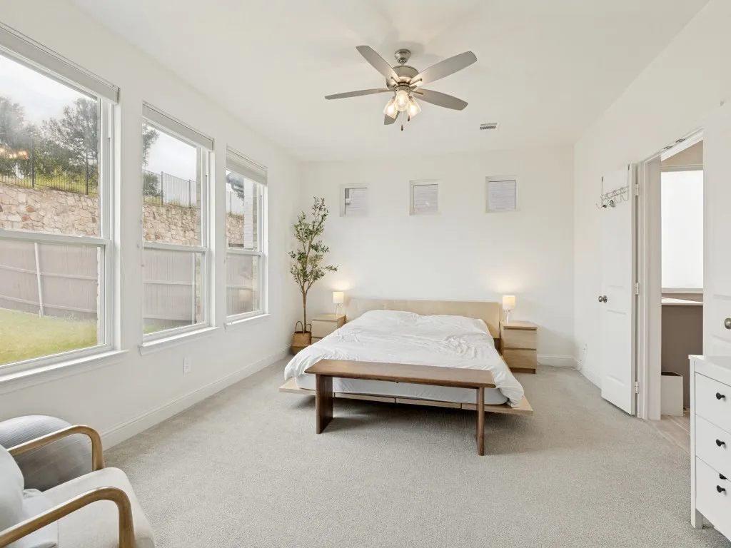 Carpeted room featuring a ceiling fan with integrated lighting, a wall of three large windows, and a doorway opening to an additional space