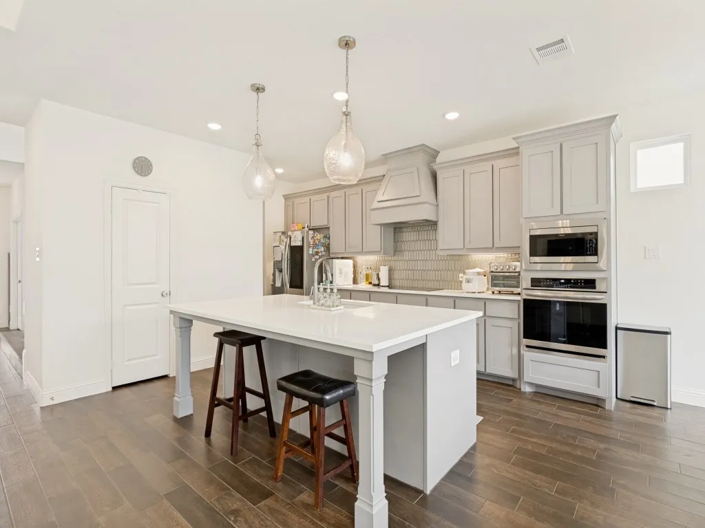 Kitchen featuring a large island with white countertop, recessed lighting, pendent lighting, light gray cabinetry, and dark wood-finish flooring