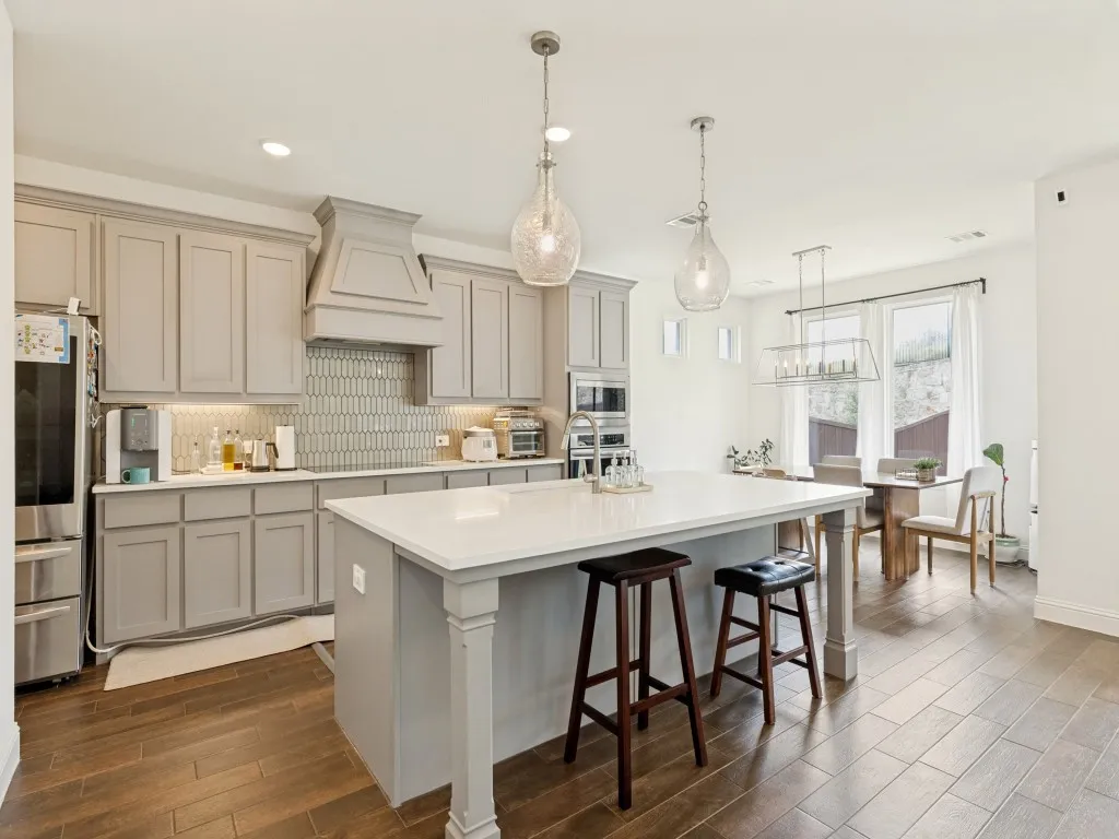 Kitchen featuring light gray cabinetry, a white countertop island with pendant lighting, stainless steel appliances, and wood-finish flooring