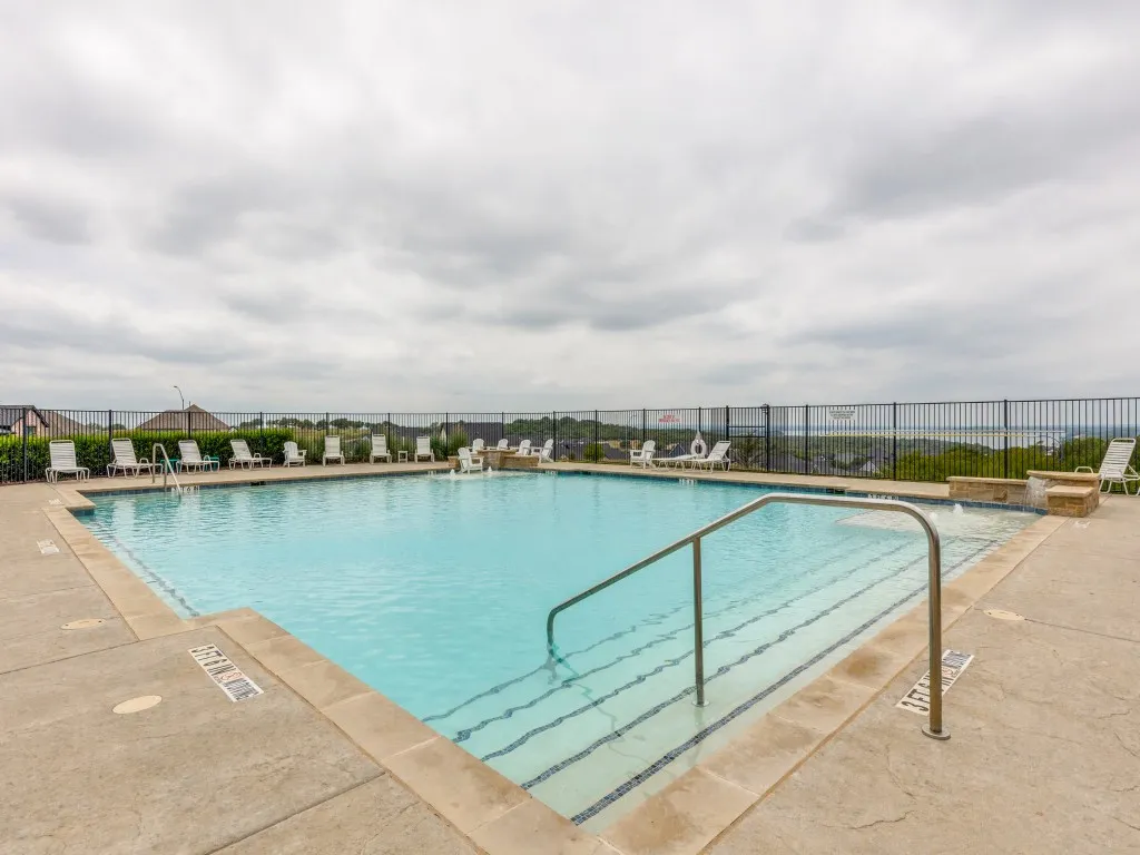 Community swimming pool featuring a concrete deck surround, integrated steps with handrails, and a dedicated water feature