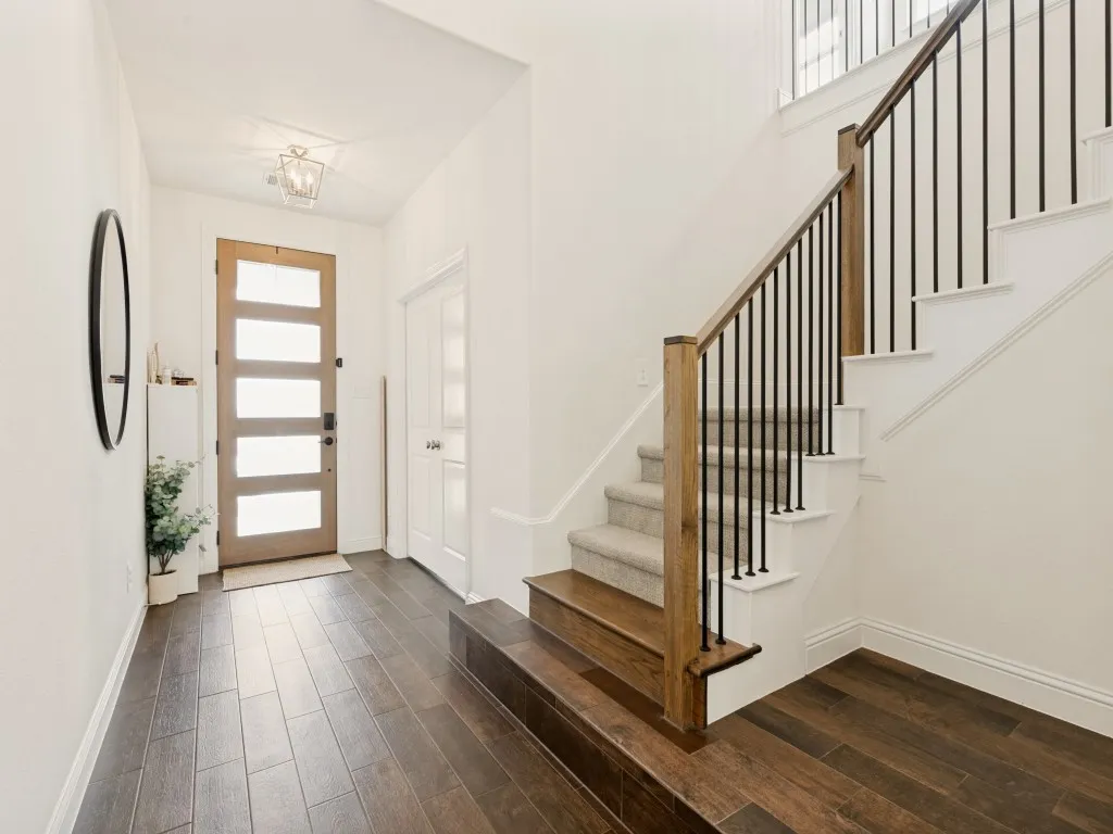 Foyer featuring wood-finish flooring, a contemporary wood front door with frosted glass panels, a carpeted staircase with wood handrails and black metal balusters, and a decorative ceiling light fixture