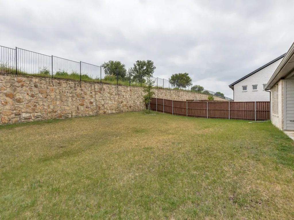 Expansive backyard featuring a stone retaining wall with black metal fencing, a wooden privacy fence, and a manicured lawn