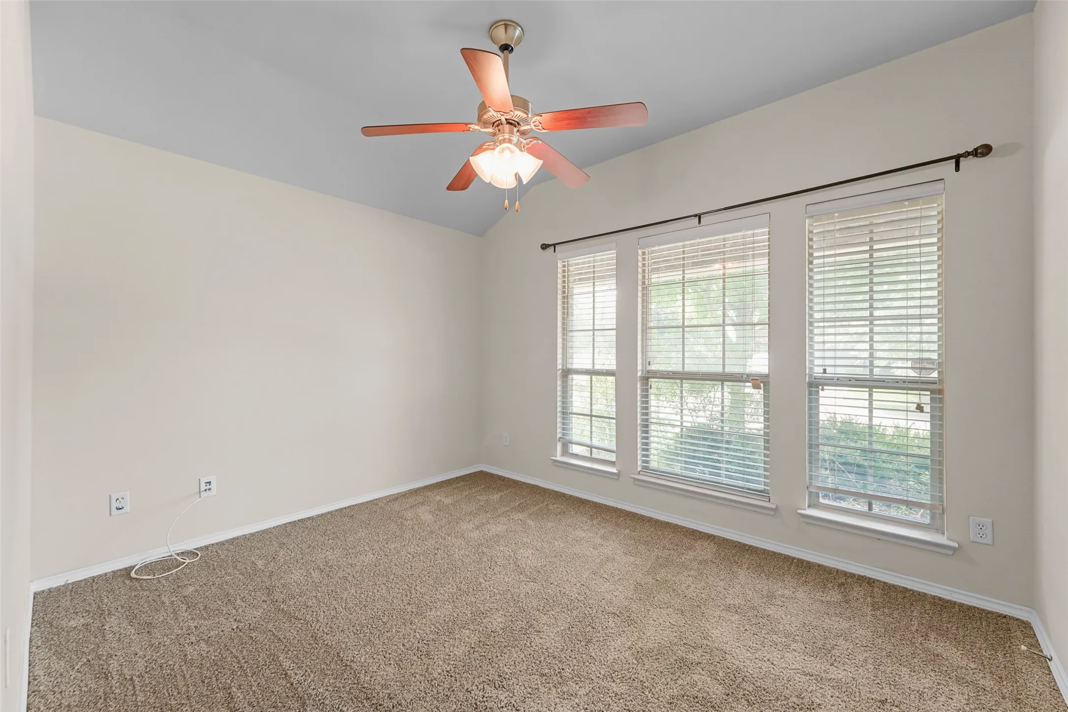 Room featuring vaulted ceilings, neutral wall tones, carpet flooring, a ceiling fan with integrated lighting, and three tall windows with horizontal blinds