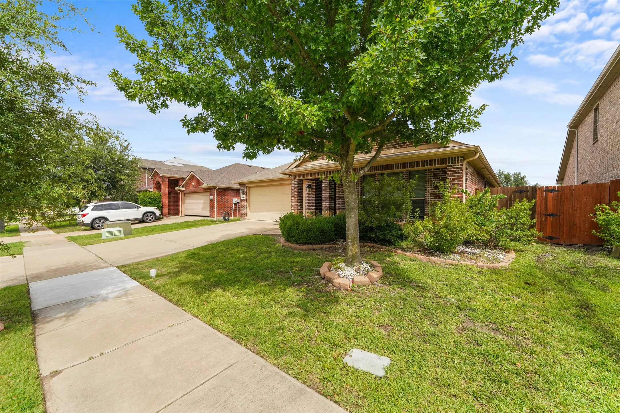 Brick exterior featuring an attached garage, landscaped front yard with mature tree, and concrete driveway