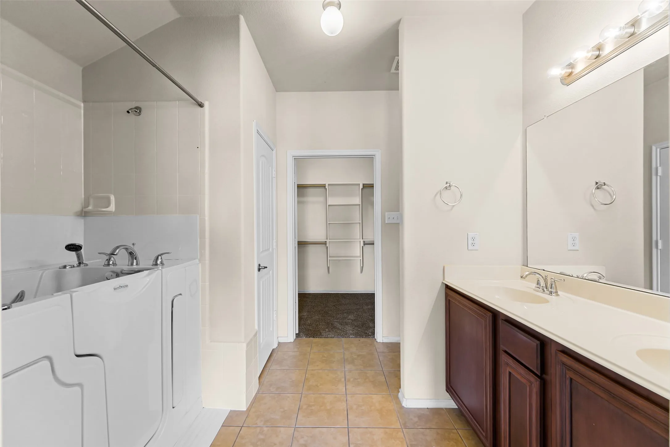 Bathroom with a walk-in tub, dual vanity with undermount sinks, and a framed mirror