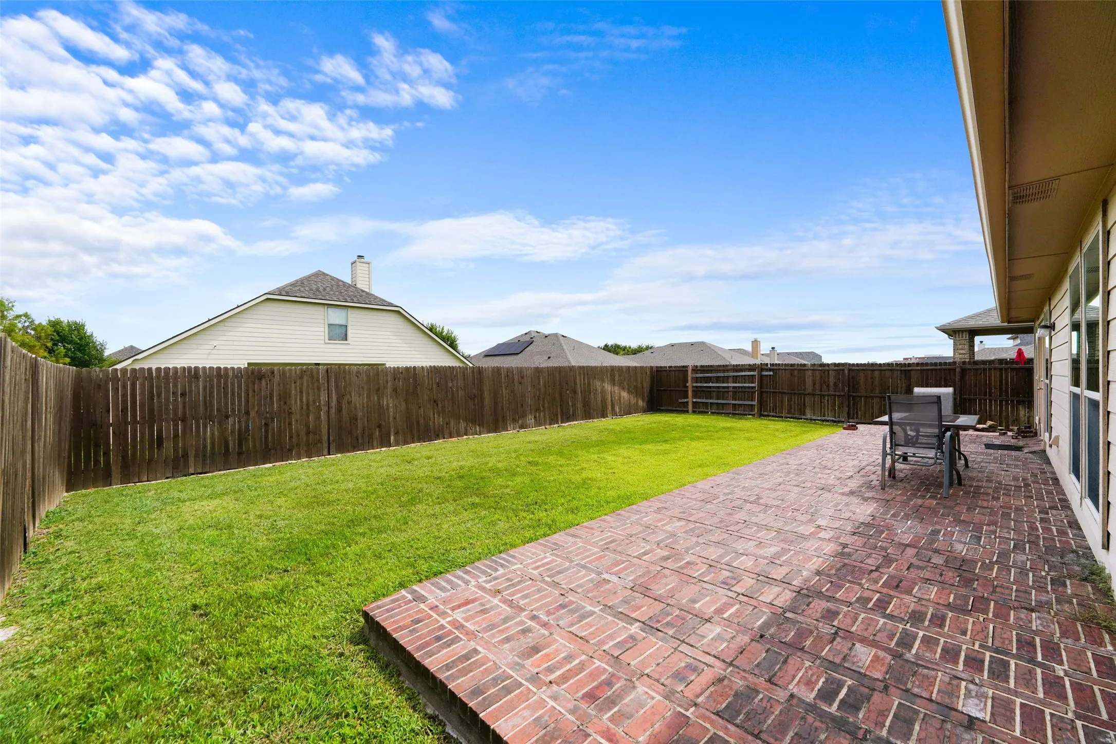 Expansive backyard featuring a brick paver patio, a manicured lawn, and a wood privacy fence