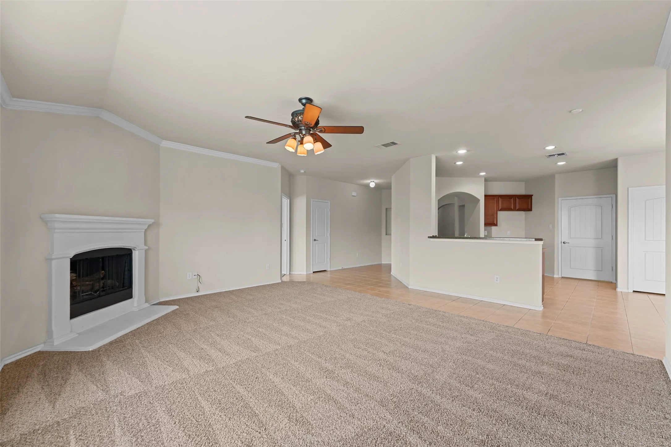 Spacious living area featuring a corner fireplace with a white mantel, textured carpeting, and a ceiling fan with integrated lighting