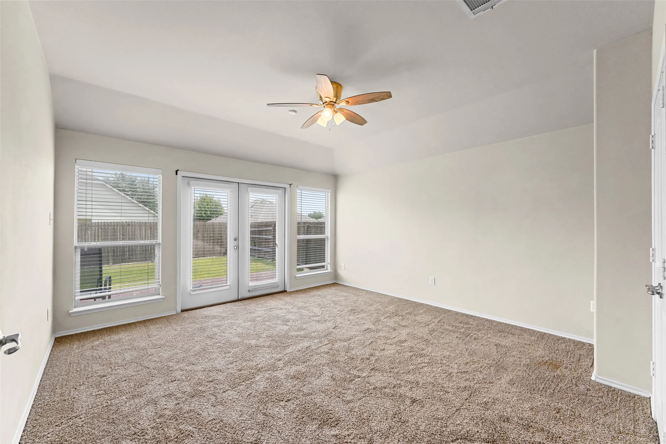 Carpeted room featuring a ceiling fan, white wall paint, and double patio doors with side windows leading to a fenced backyard