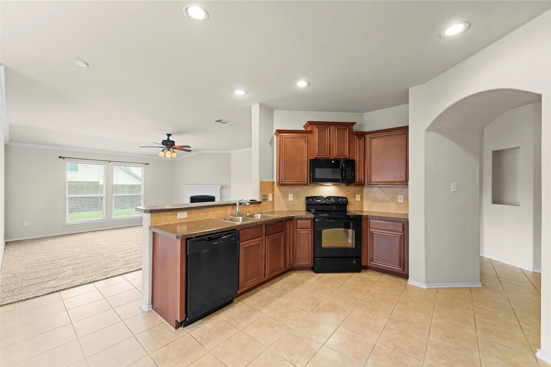 Kitchen featuring L-shaped wood cabinetry, a tile backsplash, black appliances, and a breakfast bar