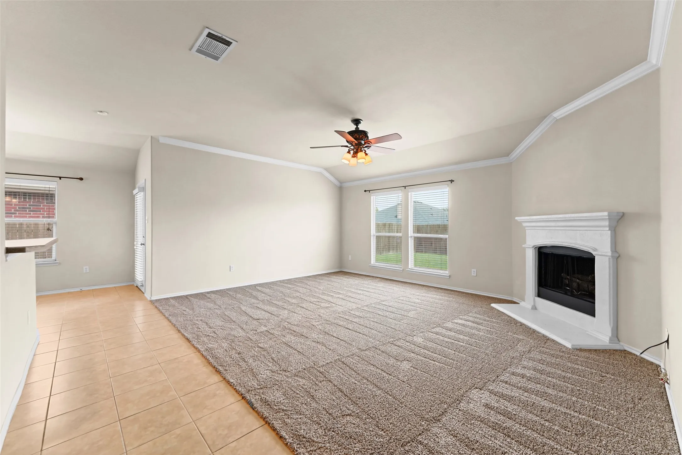 Spacious living area featuring a decorative fireplace with white mantel, vaulted ceiling with crown molding, and a ceiling fan