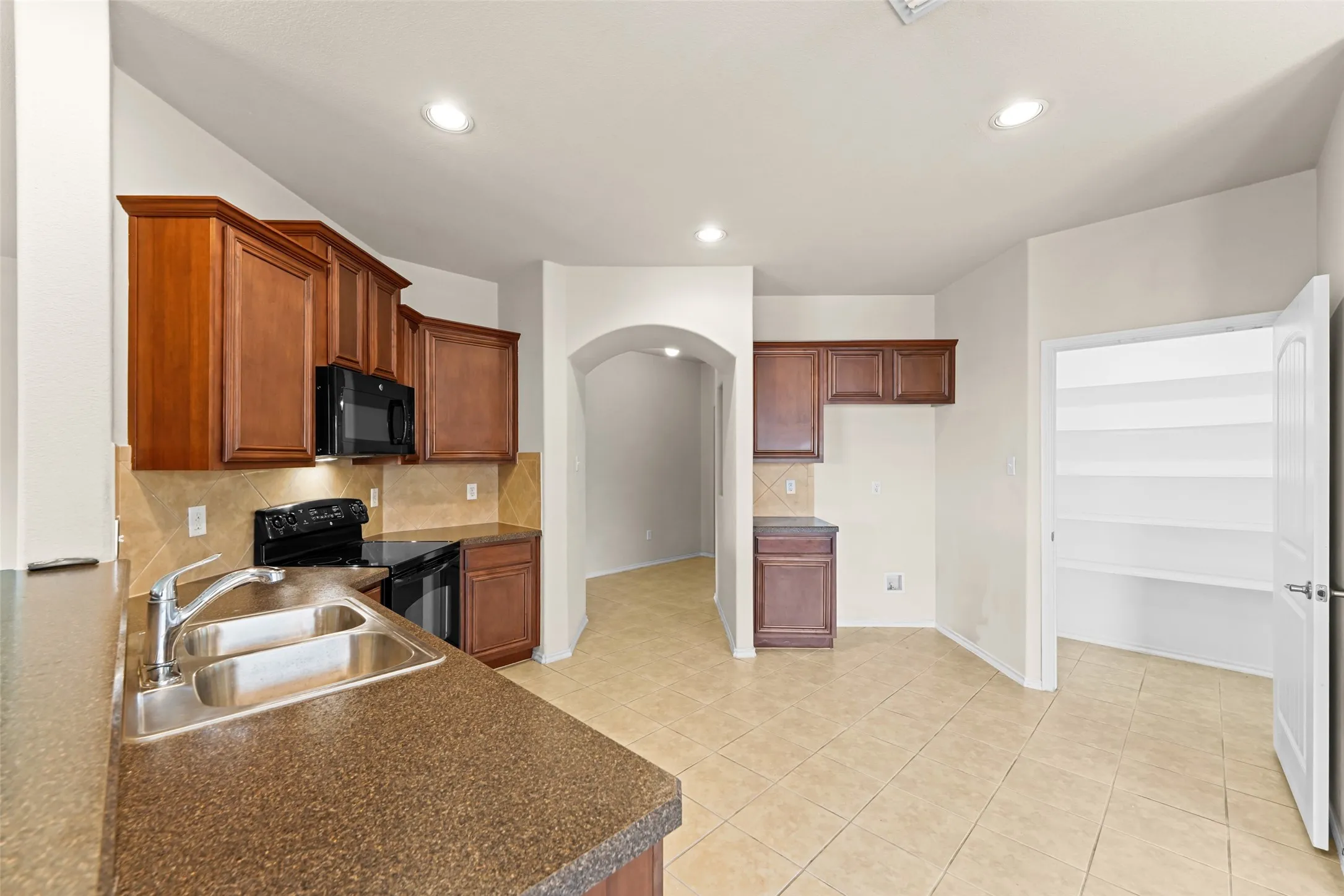 Kitchen featuring wood-finish cabinetry, black appliances, a double basin sink, and tile flooring
