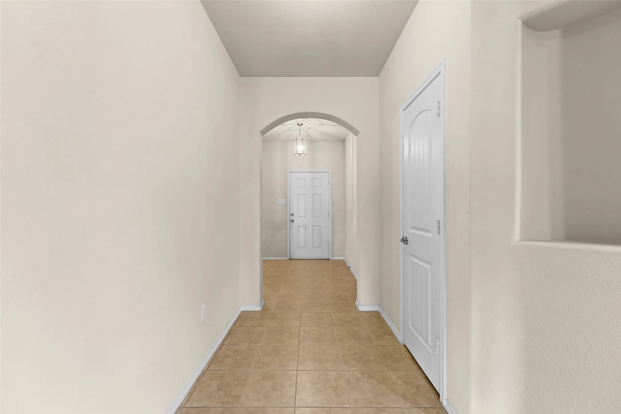 Entry hallway featuring tile flooring, neutral wall tones, an arched doorway, a built-in wall niche, and a white paneled door