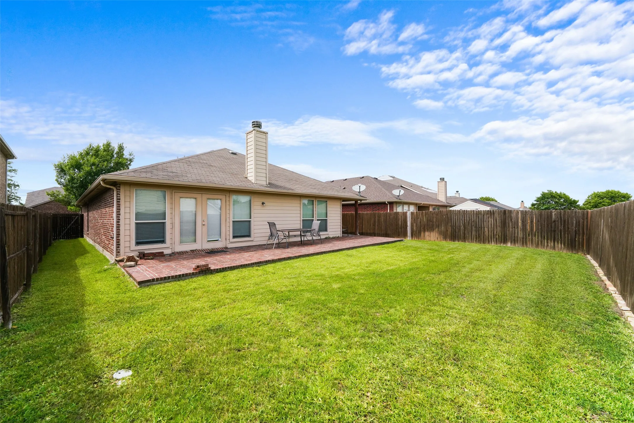 Expansive backyard featuring a brick patio, dual glass-paned doors, multiple windows, and privacy fencing