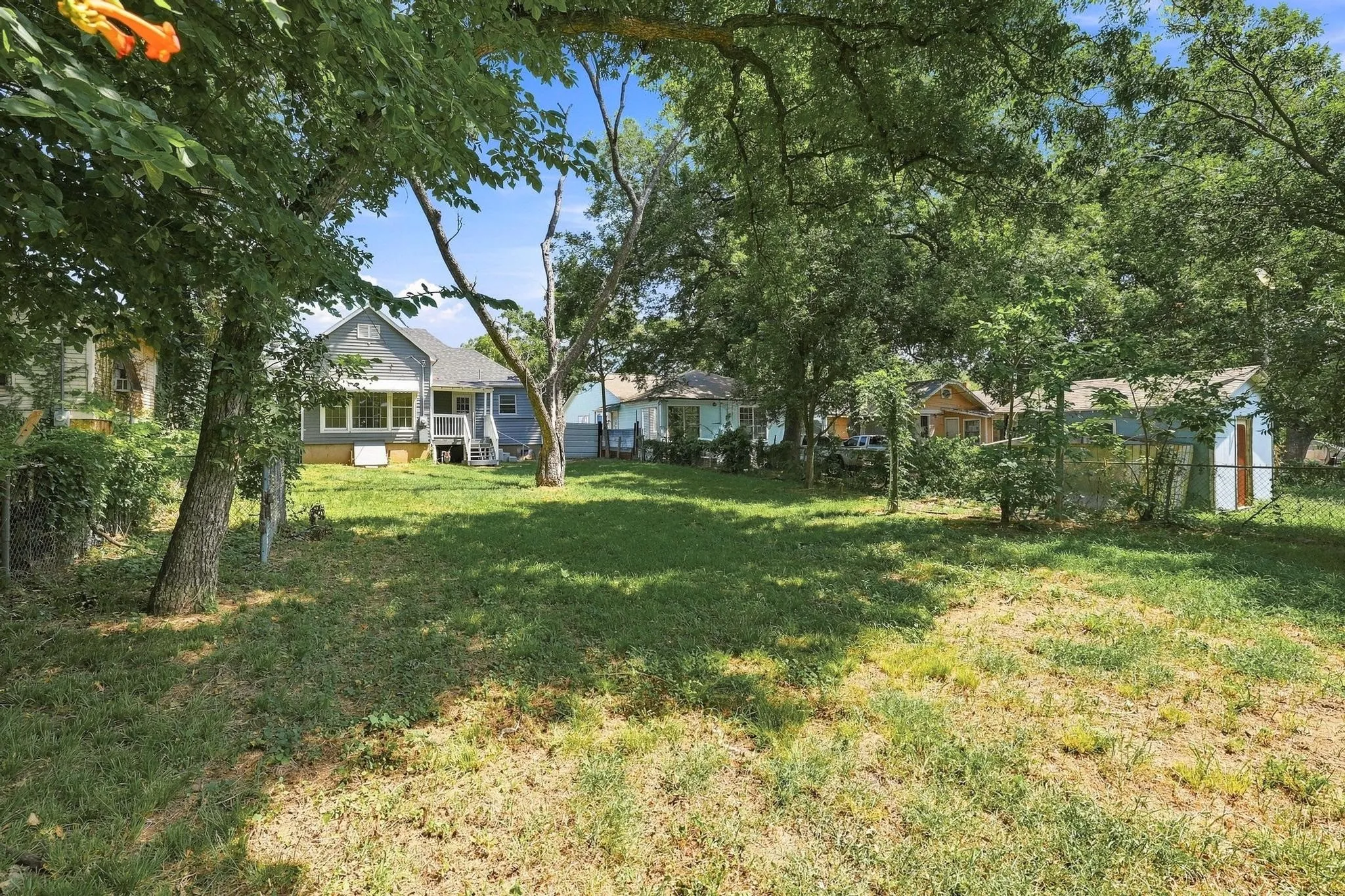 Expansive green space featuring mature trees and a chain-link fence