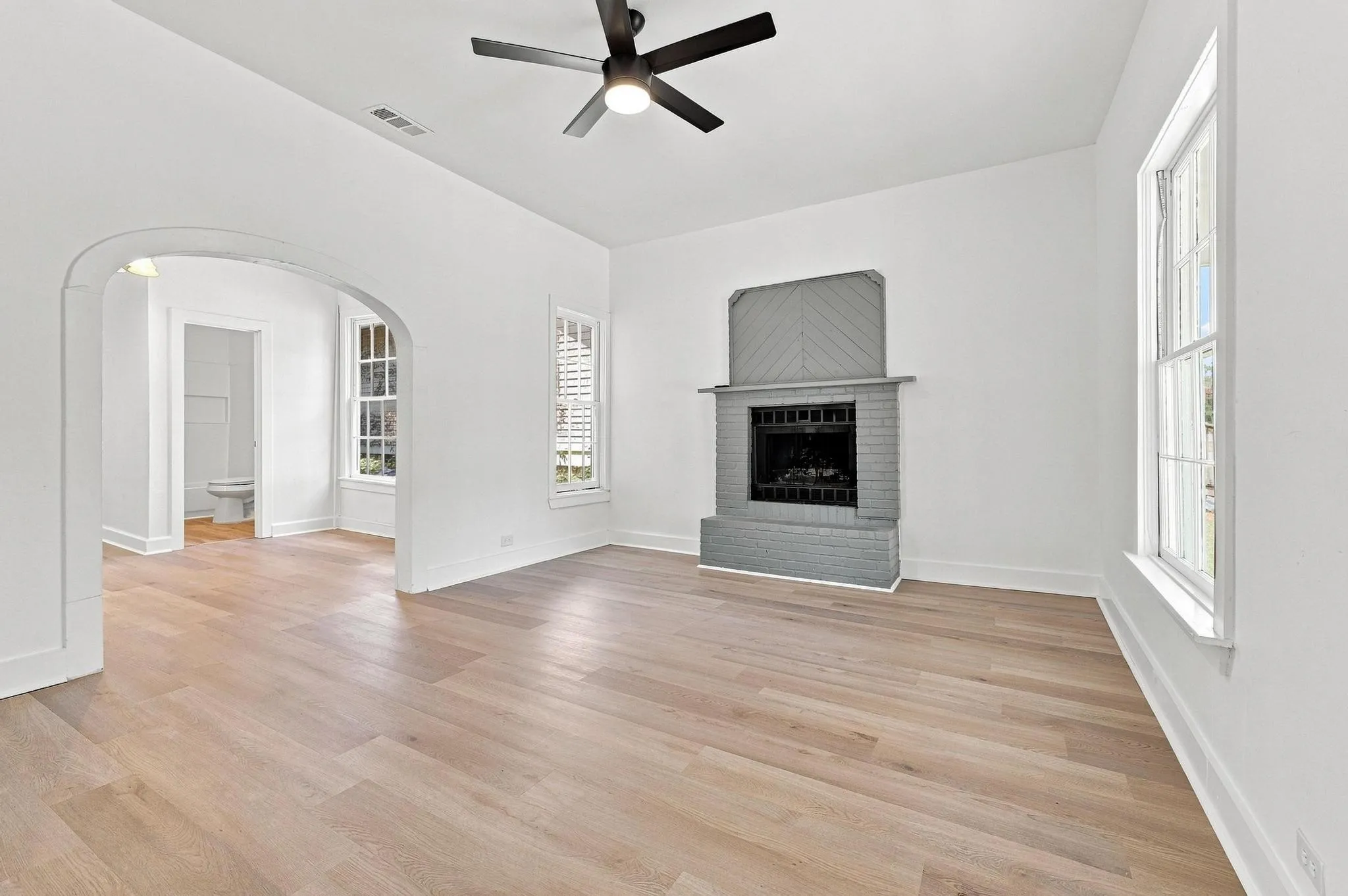Spacious living area featuring wood-finish flooring, a contemporary ceiling fan, and a fireplace with a gray brick surround