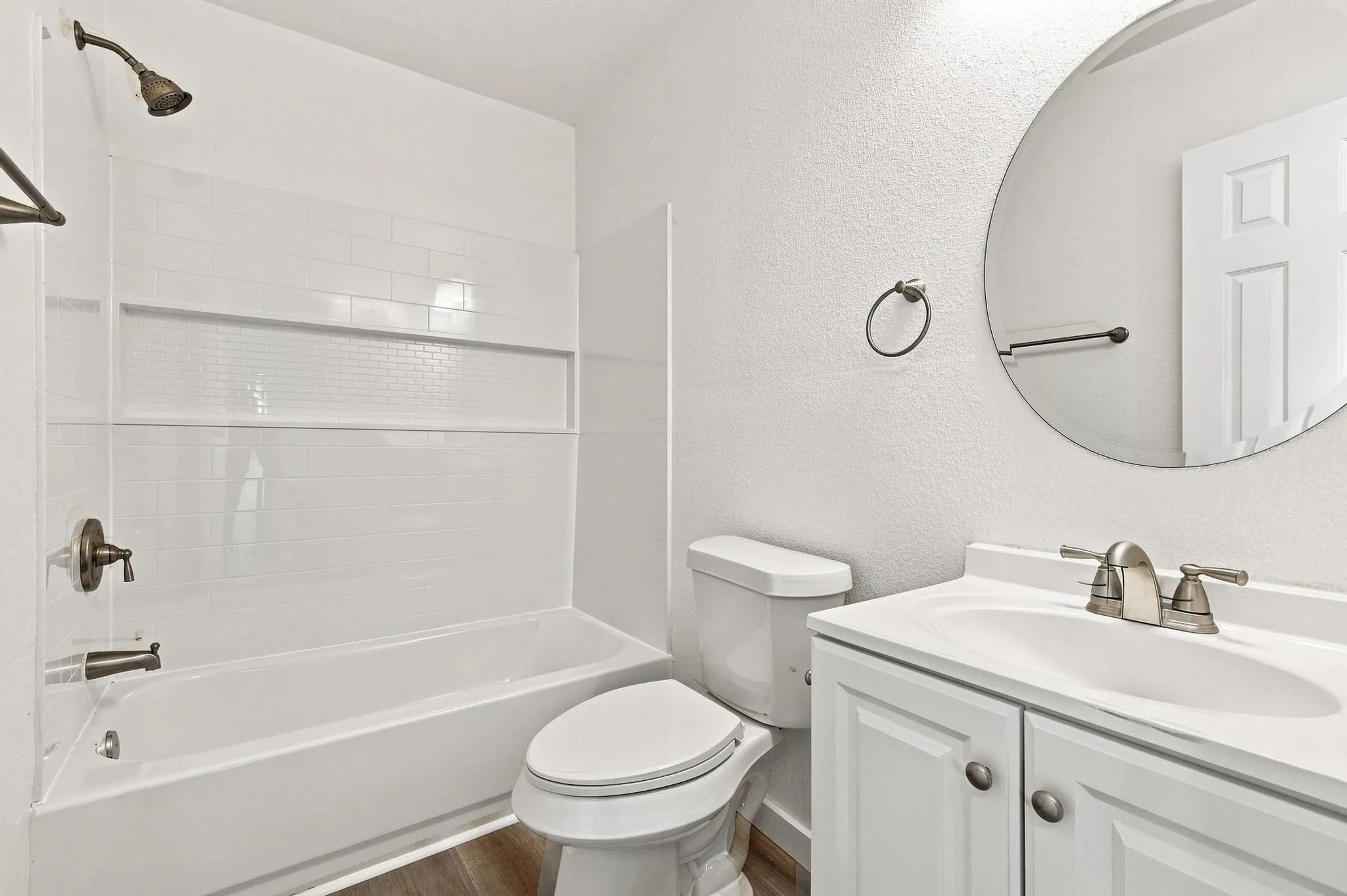 Bathroom featuring a white subway tile shower surround with a mosaic accent band, a soaking tub, a white vanity with a single basin sink, and wood-finish flooring