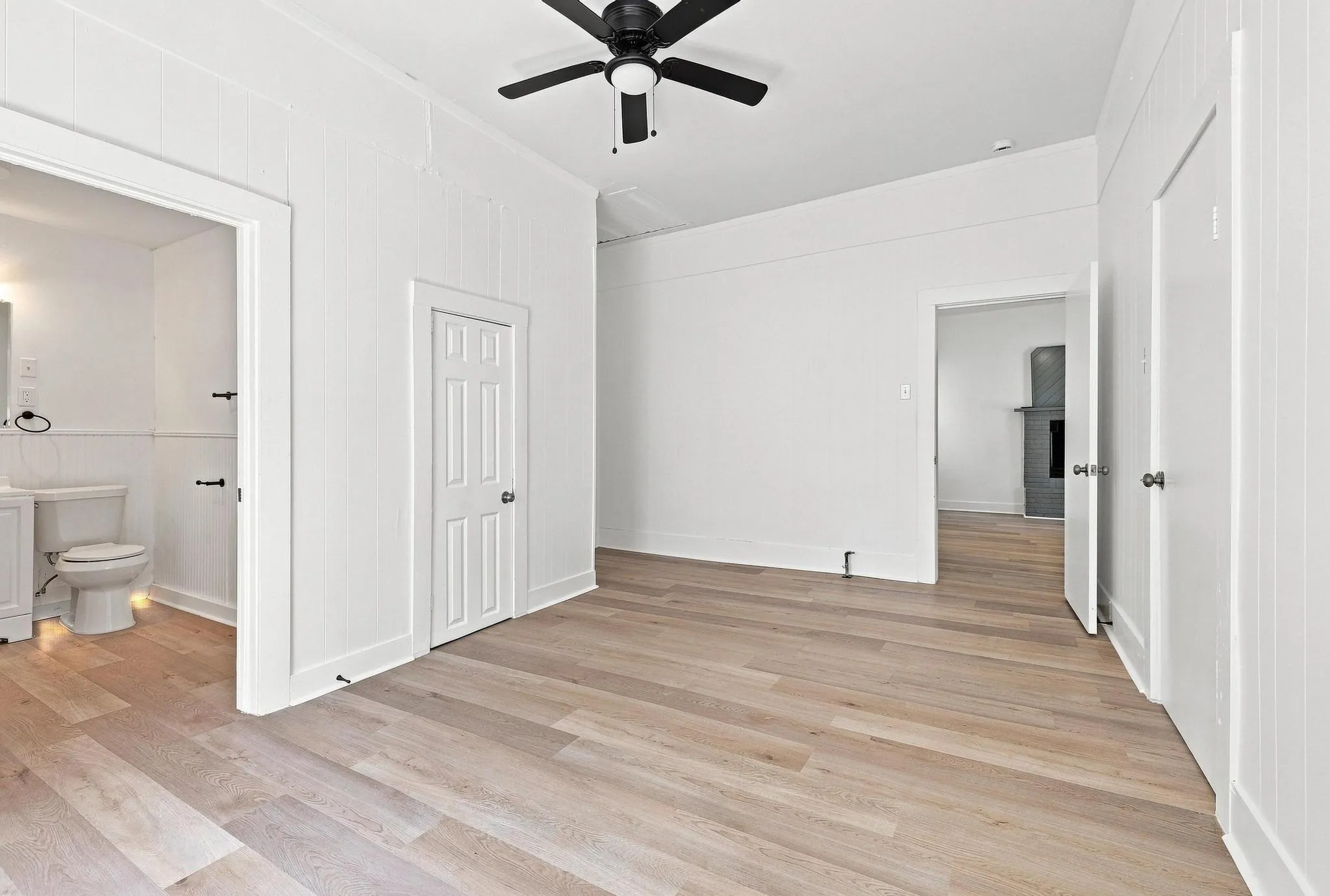 Spacious room featuring light wood-finish flooring, a ceiling fan, and crisp white walls