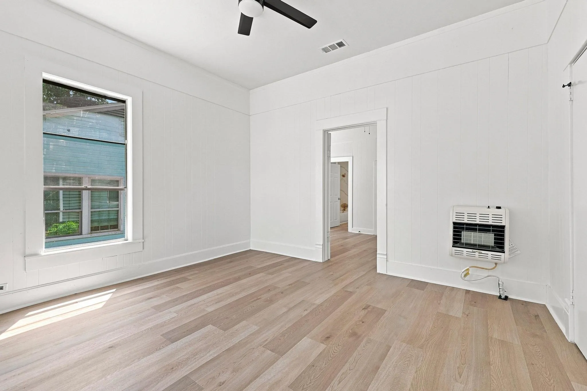 Room featuring light wood-finish flooring, white paneled walls, and a ceiling fan