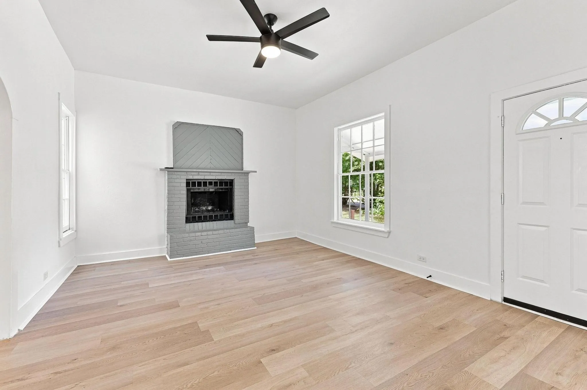 Spacious living area featuring wood-finish flooring, a contemporary ceiling fan, and a fireplace with a gray brick surround