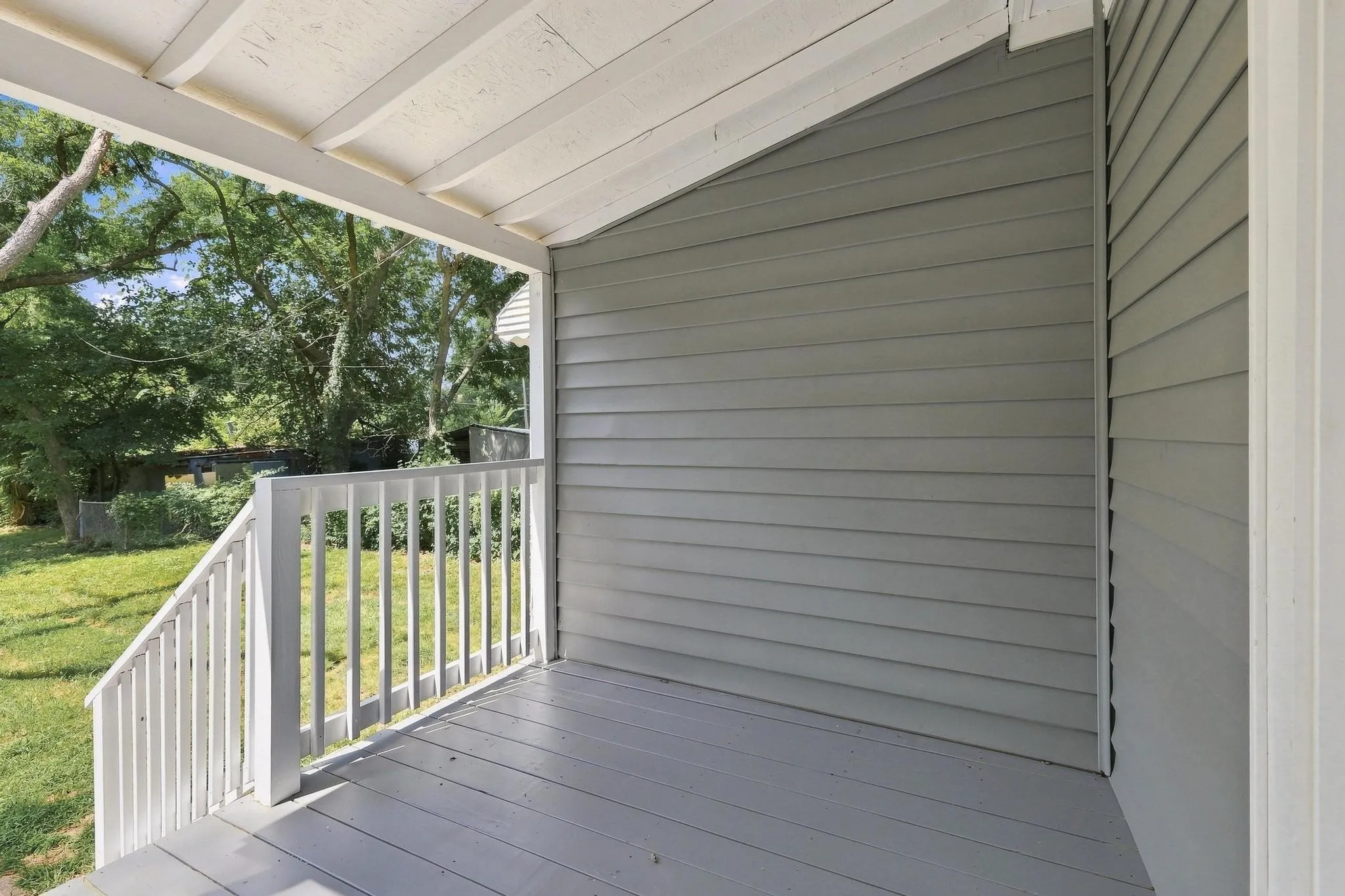 Covered porch with white painted railing, gray siding, and exposed white ceiling joists