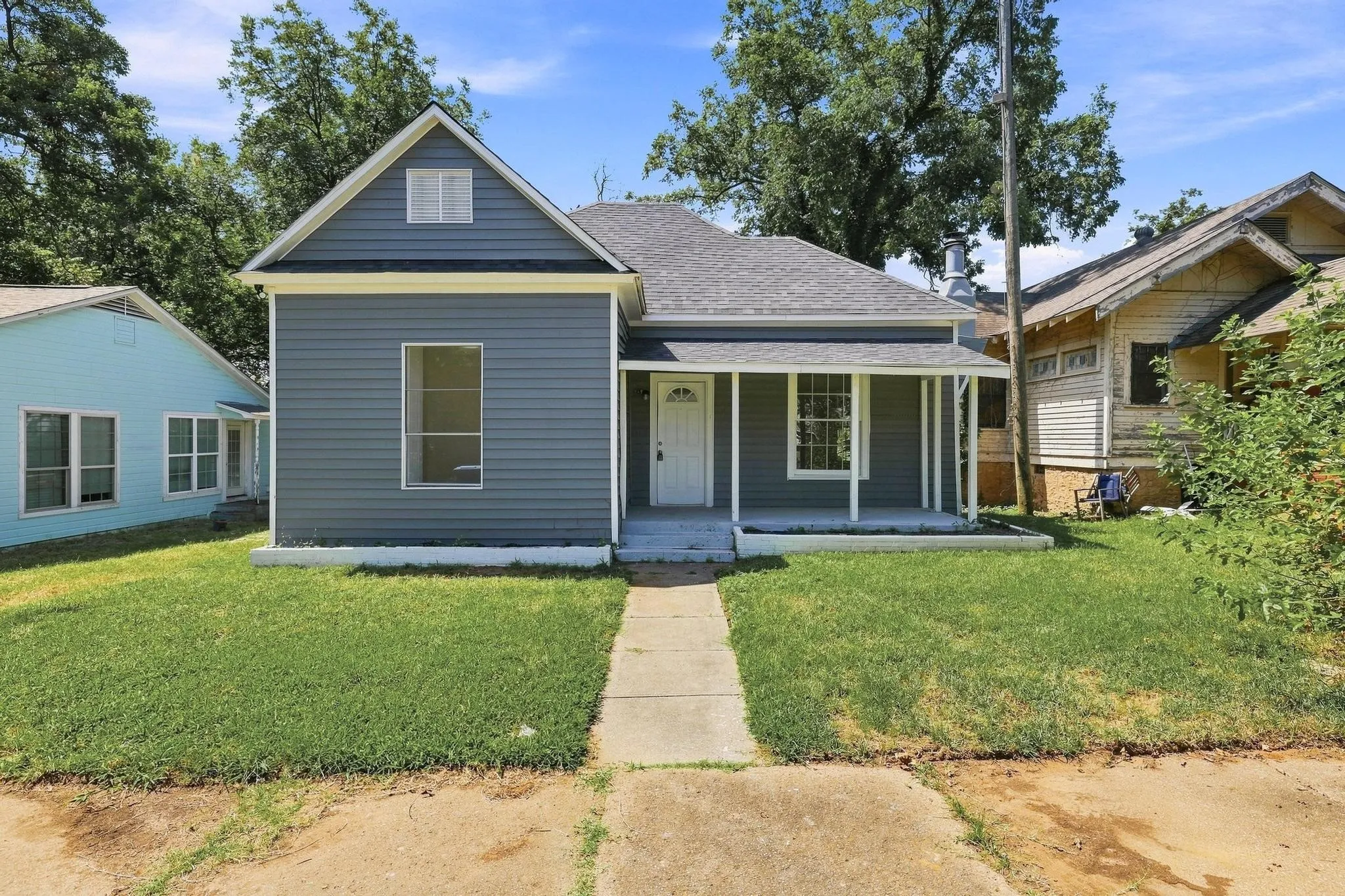 Updated front exterior with attractive gray siding, white trim, a covered front porch, newer composition roof, mature trees, large windows, and excellent curb appeal.  A welcoming entrance creates an inviting first impression.