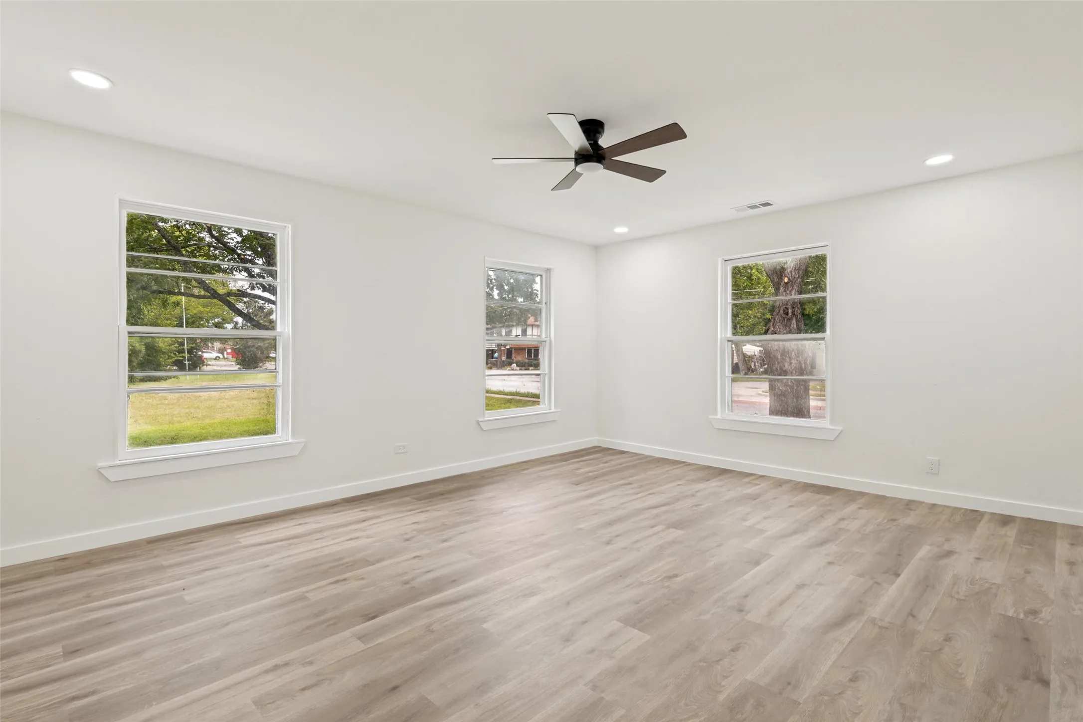 Spacious room featuring light wood-finish flooring, recessed lighting, and a contemporary ceiling fan