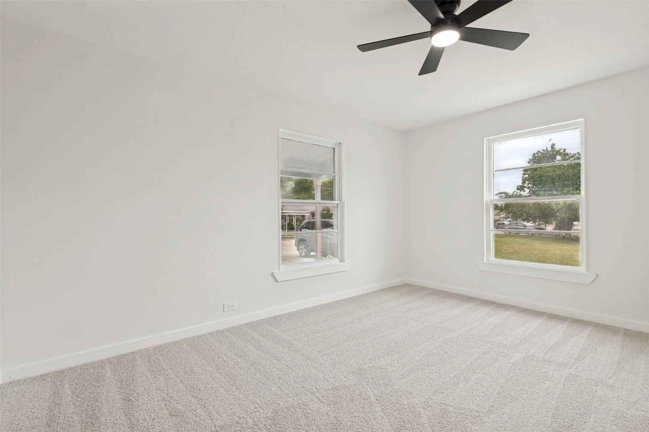 Carpeted room with two large windows and a ceiling fan with integrated lighting