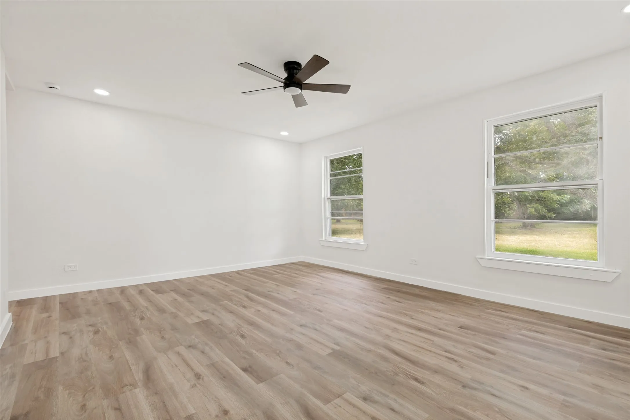 Spacious interior featuring wood-finish flooring, two large windows, a ceiling fan, recessed lighting, and white baseboards