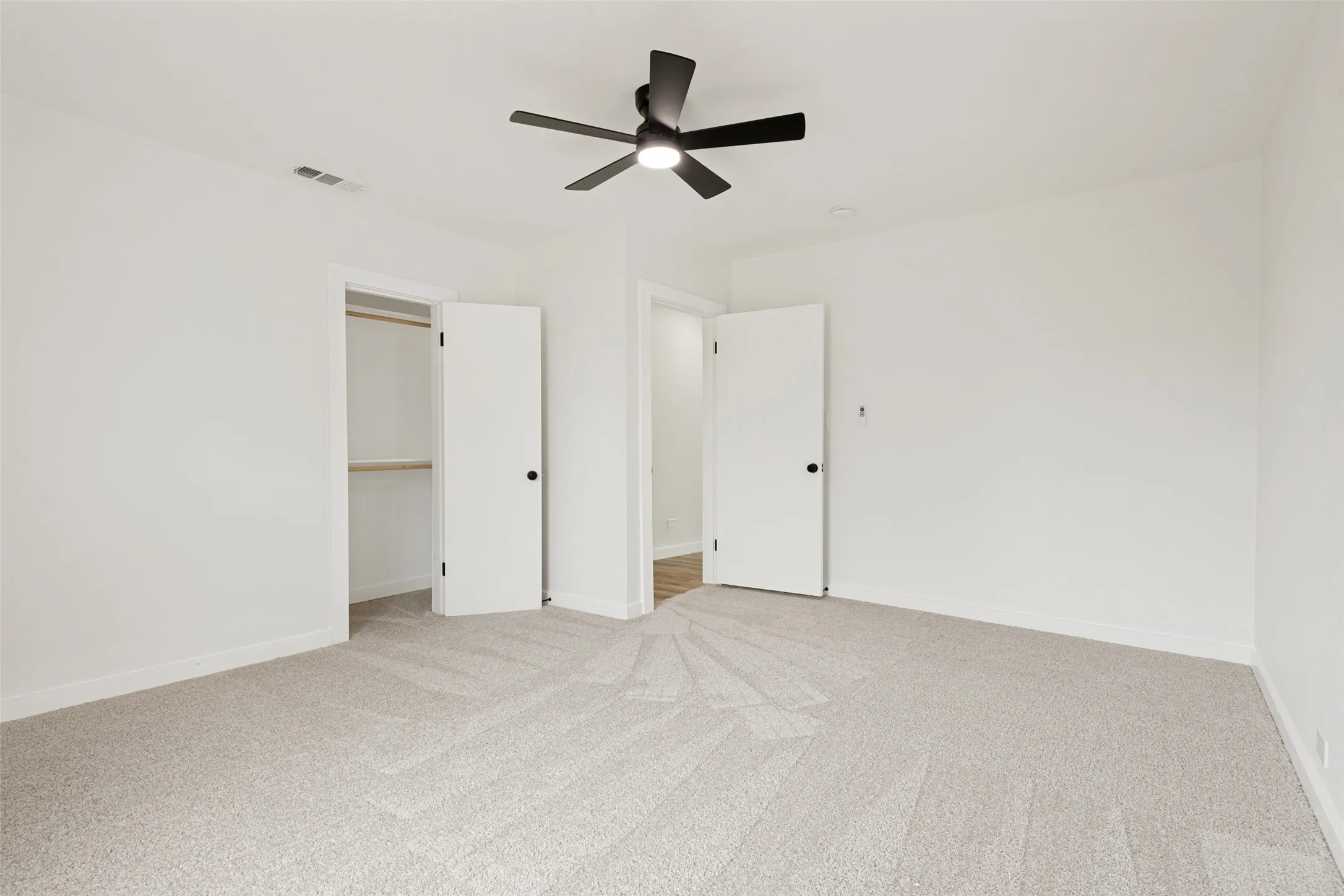 Neutral-toned carpeted room featuring a ceiling fan with black blades, white walls, and white trim