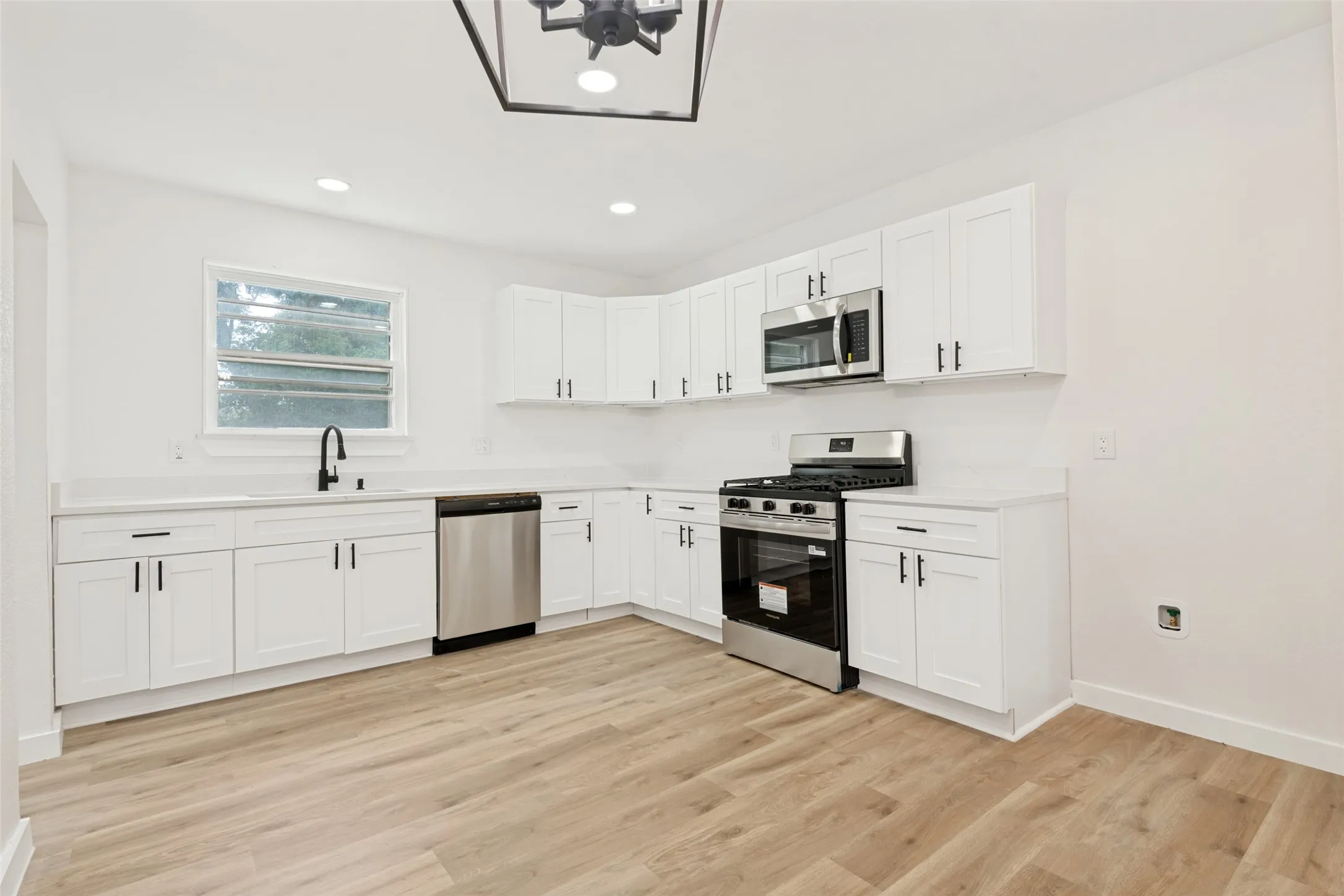 Contemporary kitchen featuring white cabinetry, light-toned countertops, stainless steel appliances, and wood-finish flooring