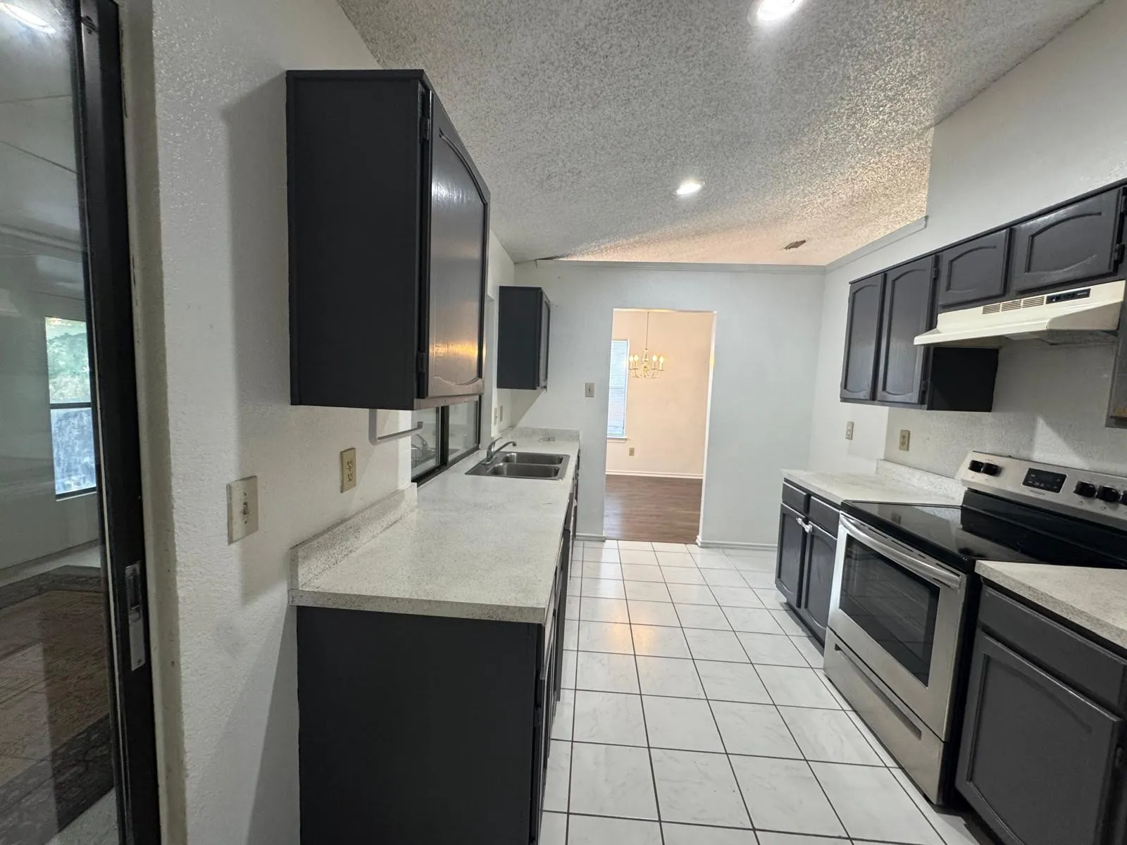 Kitchen featuring dark cabinetry, light-toned countertops, a stainless steel electric range, a dual basin sink, and white tile flooring