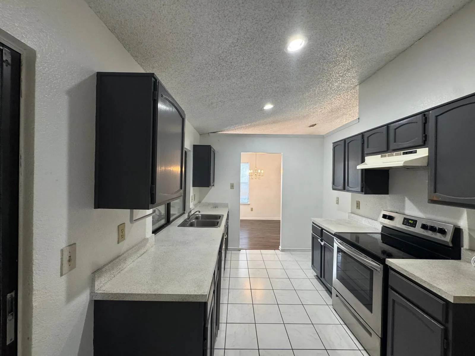 Galley kitchen featuring dark cabinetry, light countertops, a stainless steel range, a white tile floor, and recessed lighting