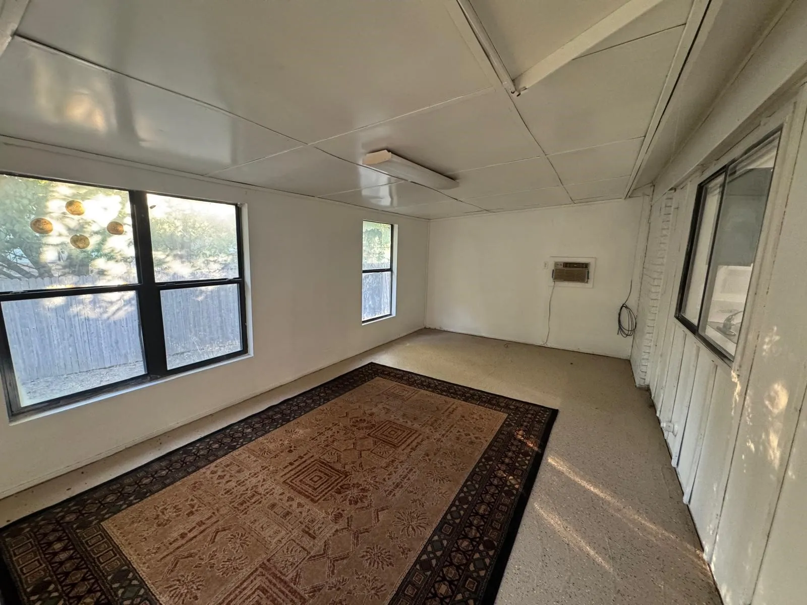 Spacious room featuring multiple windows, a wall-mounted air conditioning unit, and light-colored flooring