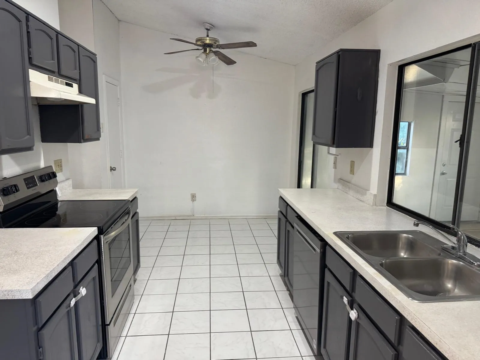 Kitchen featuring white square tile flooring, dark cabinetry, light countertops, and stainless steel appliances