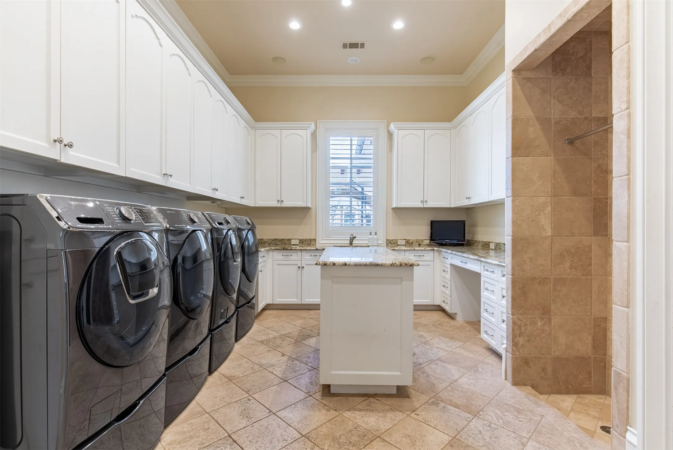 Expansive utility room featuring four front-load laundry appliances, extensive white cabinetry, granite countertops, and utility wash area