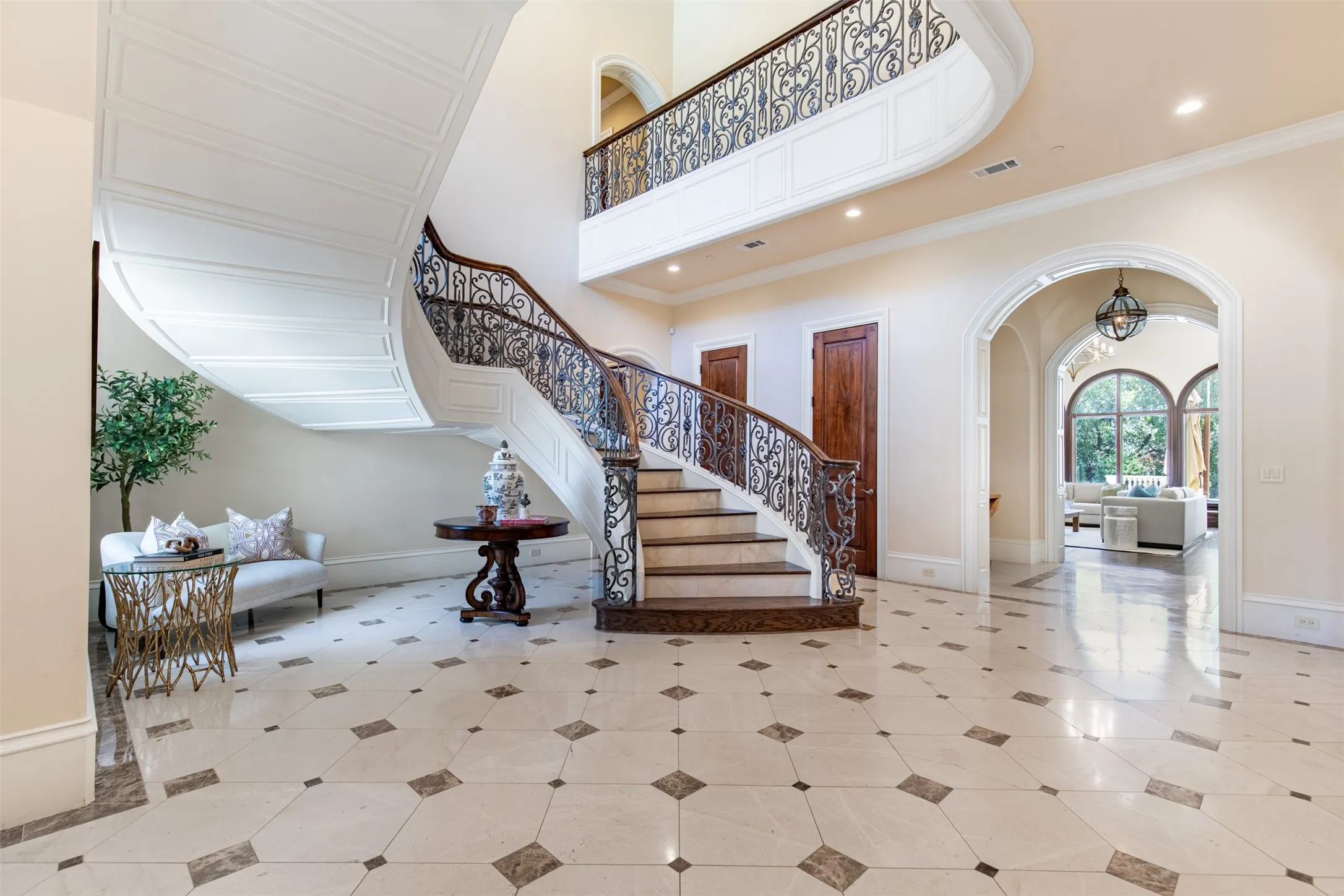 Grand two-story foyer with diamond pattern marble stone with mosaic pattern. Ornate curved iron stairway.