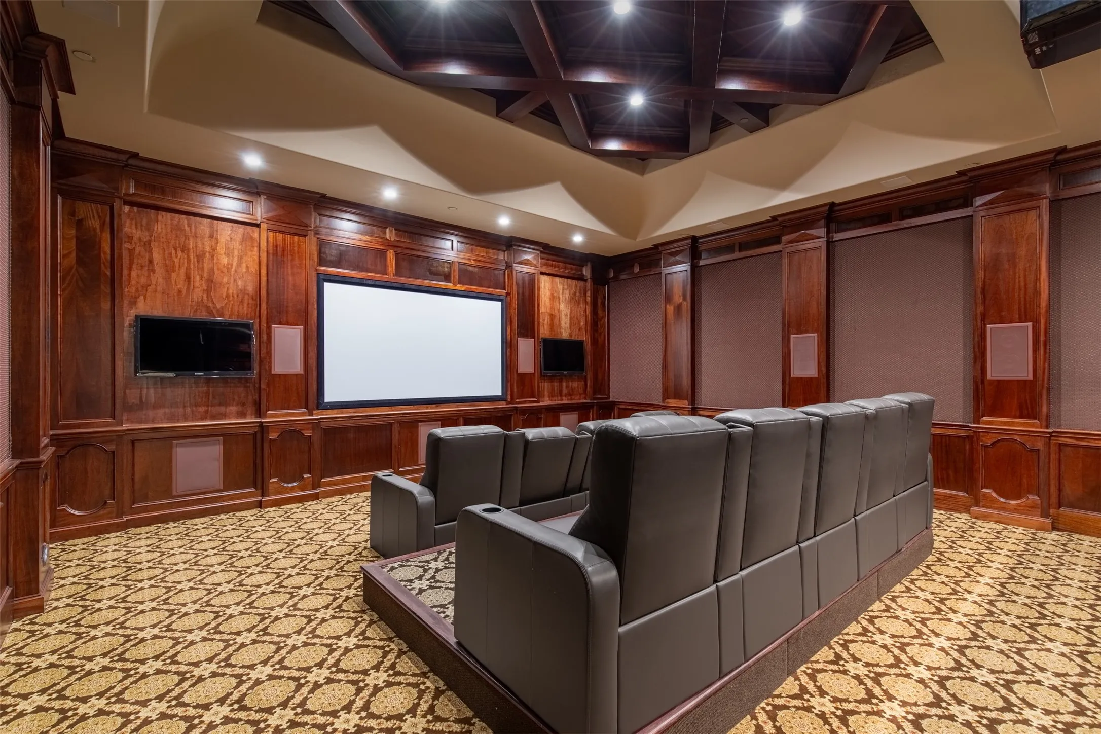 Dedicated media room featuring wood paneling, a large projection screen, two televisions, patterned carpeting, recessed lighting, and media room chairs