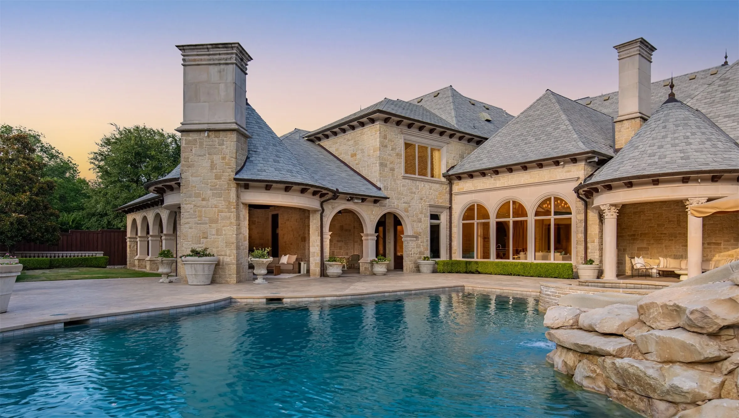 Resort-style pool area featuring a stone waterfall, extensive paved decking, and multiple covered loggias
